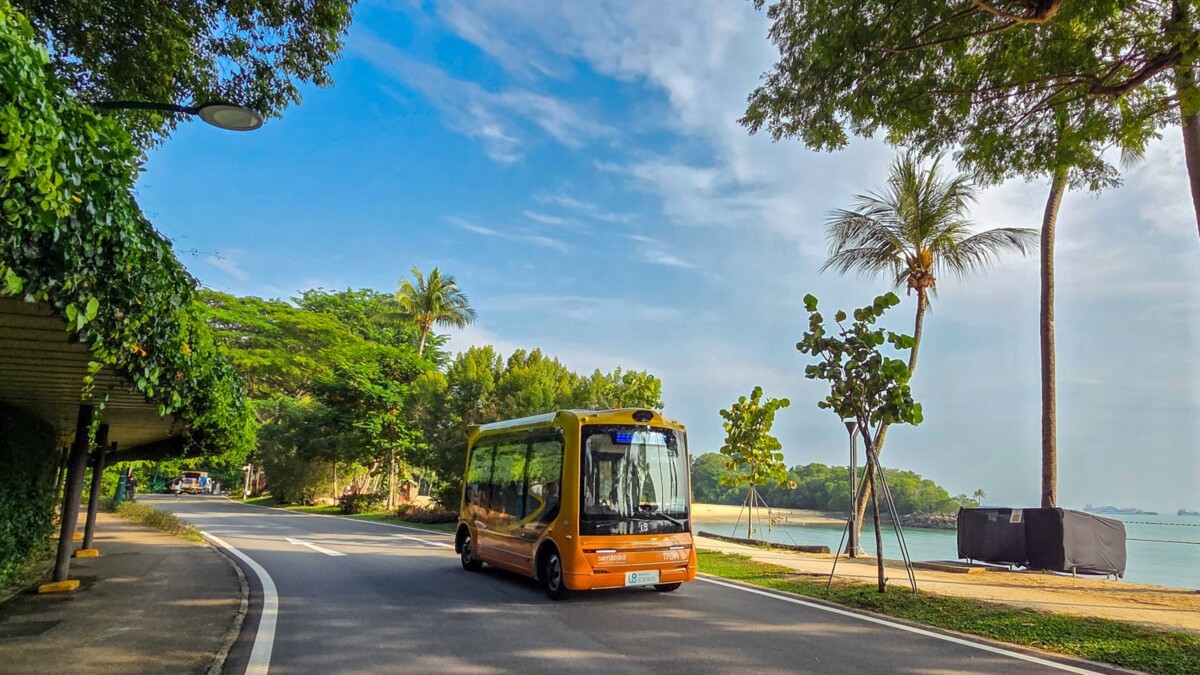 Yellow autonomous shuttle on a tree-lined Sentosa coastal road with the sea on the right