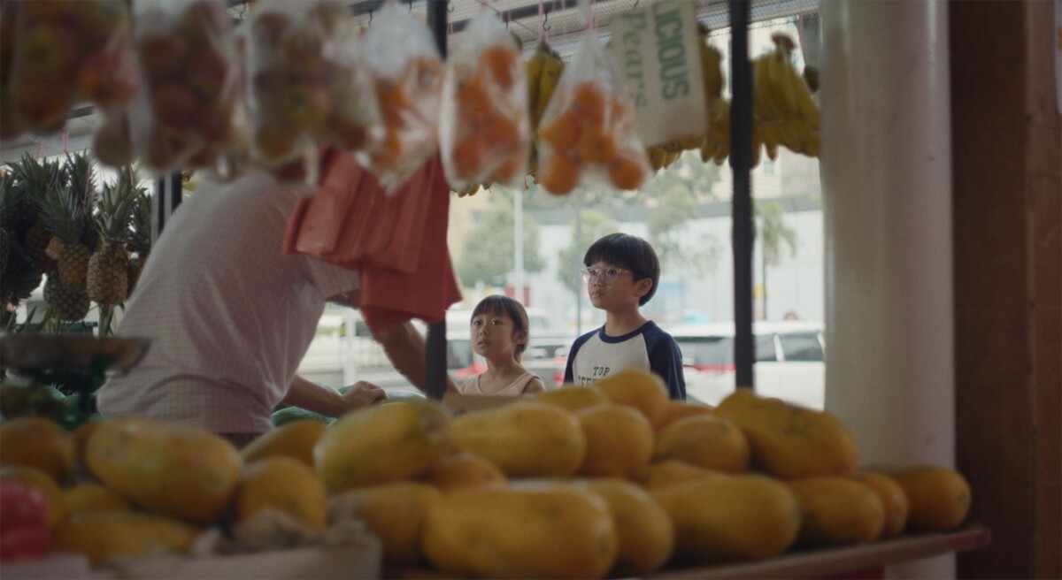 Two children walk past a fruit stall in a still from Cheryl Wong's It's Not Sweet