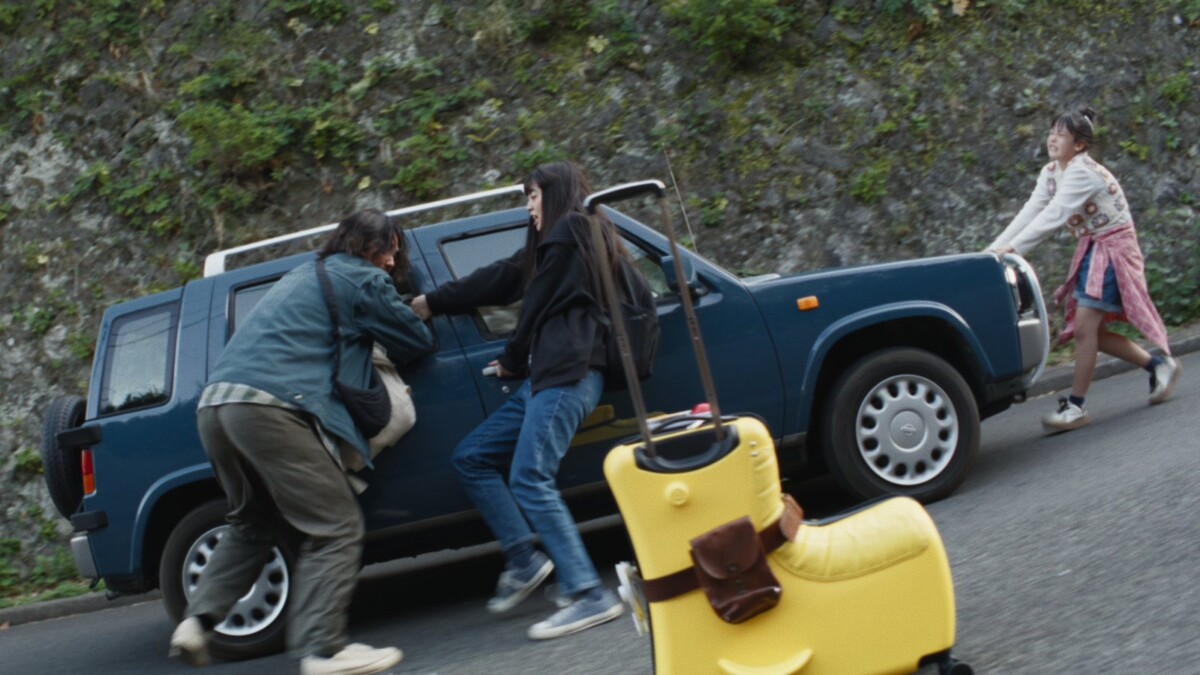 Still from The Invisibles showing a family pushing a car on a hillside road