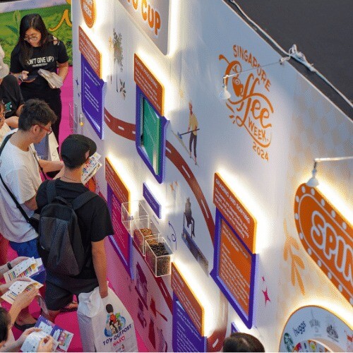 Visitors at an illuminated Singapore Coffee Week wall tracing the history of coffee with panels and displays