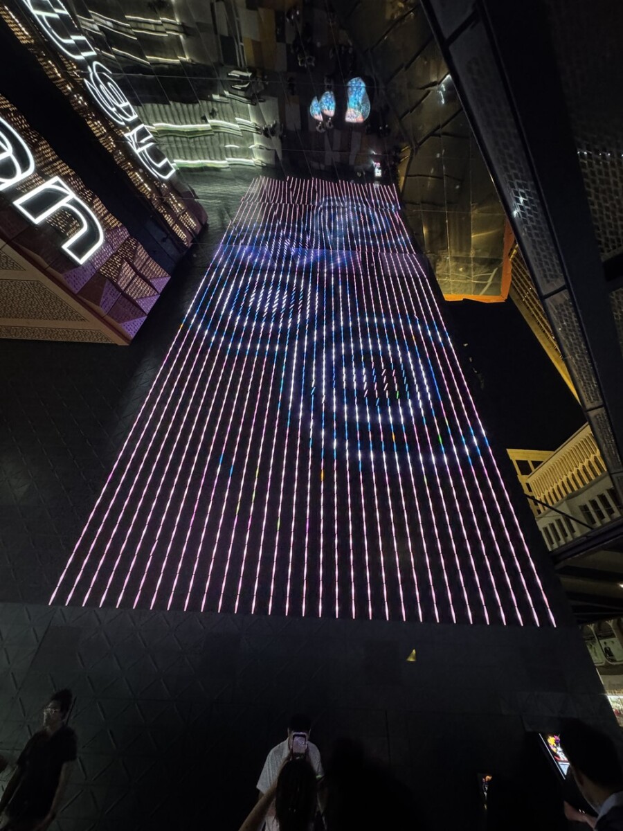A wall of glowing pink, white and blue light strands forming a kinetic art installation at Funan mall, with the mall's signage reflected in glass nearby