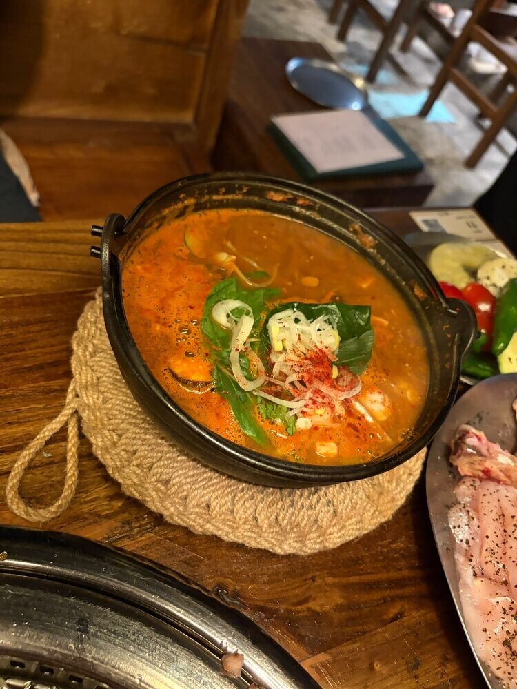 A bubbling bowl of doenjang soybean paste stew with tofu, mushroom and vegetables in a black stone pot