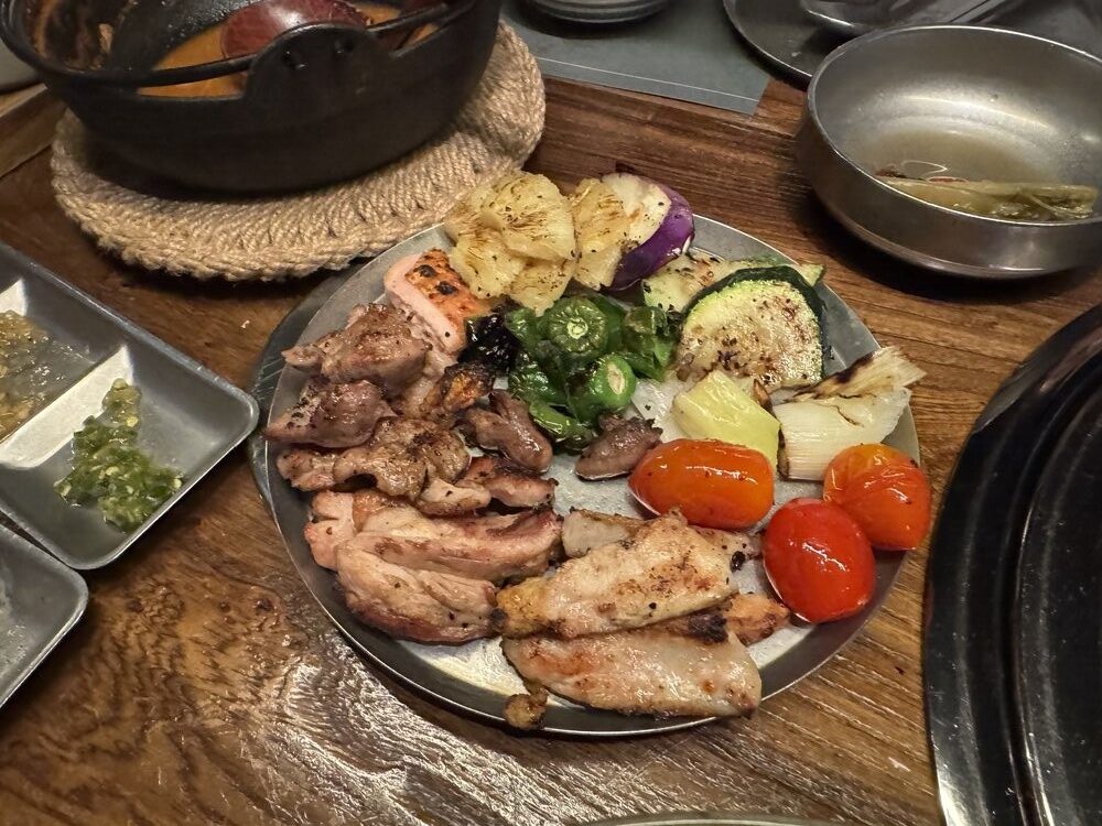 A finished platter of grilled chicken cuts, charred zucchini, shishito peppers and cherry tomatoes, alongside grilled leek and eggplant