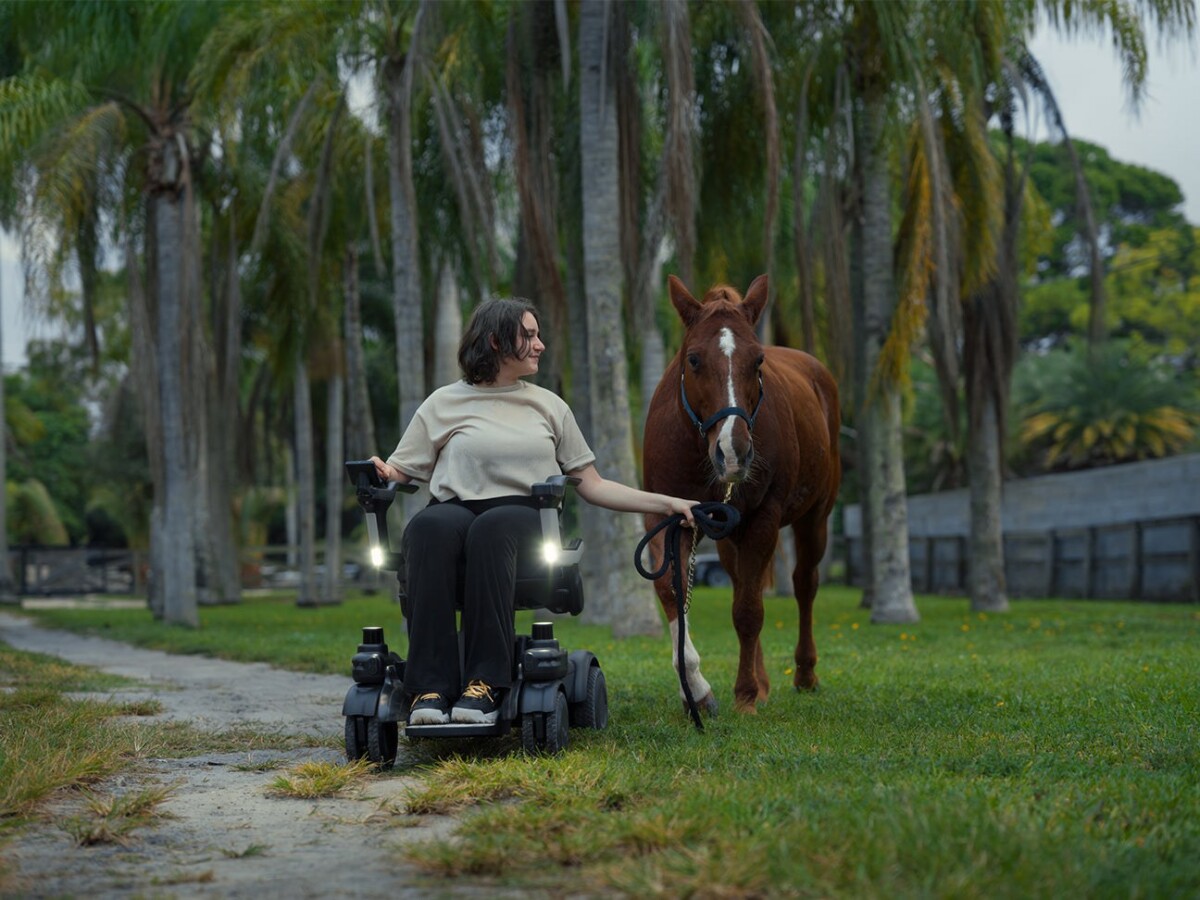 Strutt ev¹c smart power wheelchair driven outdoors on grass beside a horse