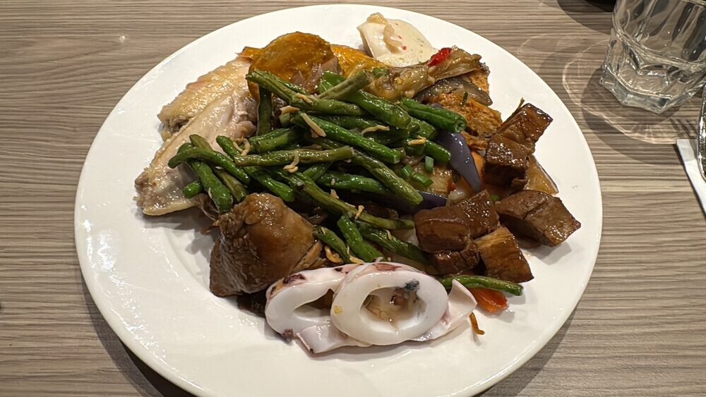 Plate of steamed chicken, long beans, braised beancurd, squid and vegetables assembled from the buffet