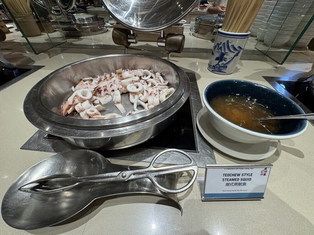 Teochew Style Steamed Squid on a serving tray with a bowl of dipping sauce and metal tongs, dish label alongside