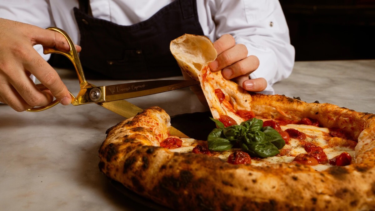 Chef cutting a tomato and basil Neapolitan pizza with gold scissors
