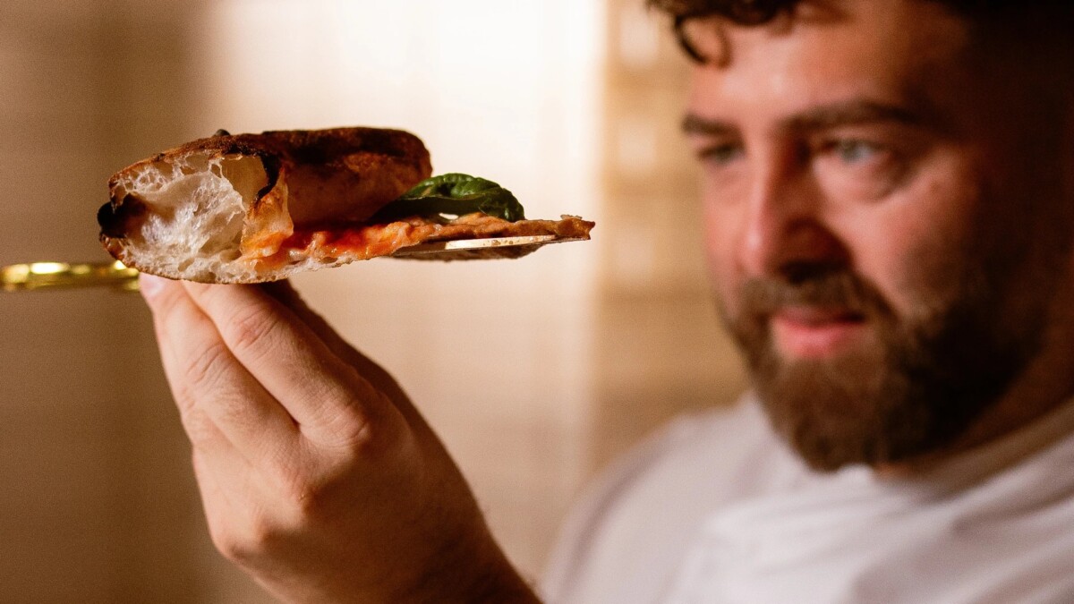 Vincenzo Capuano holding a sliced pizza with gold-handled scissors