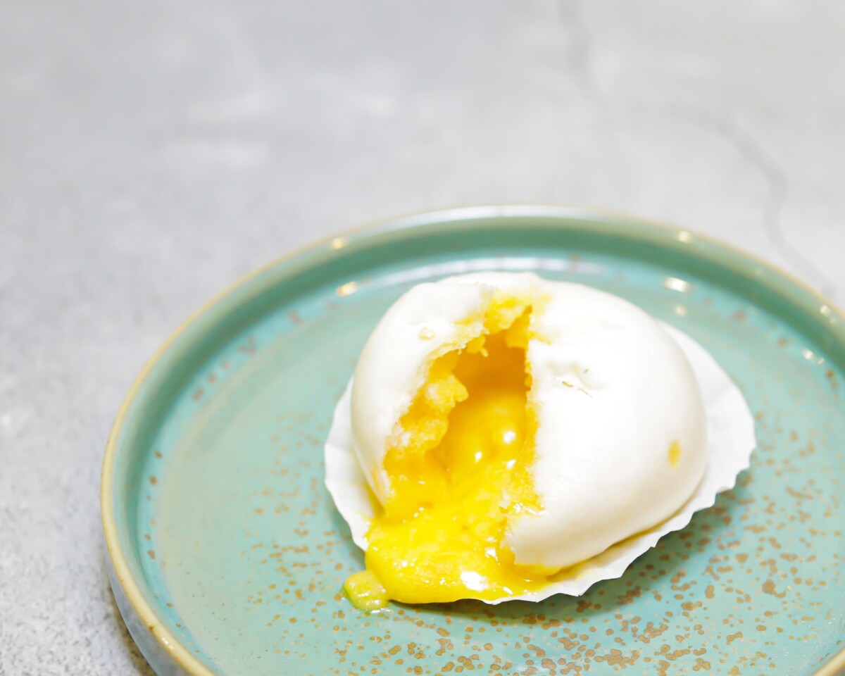 Golden egg yolk lava bun torn open with custard flowing out